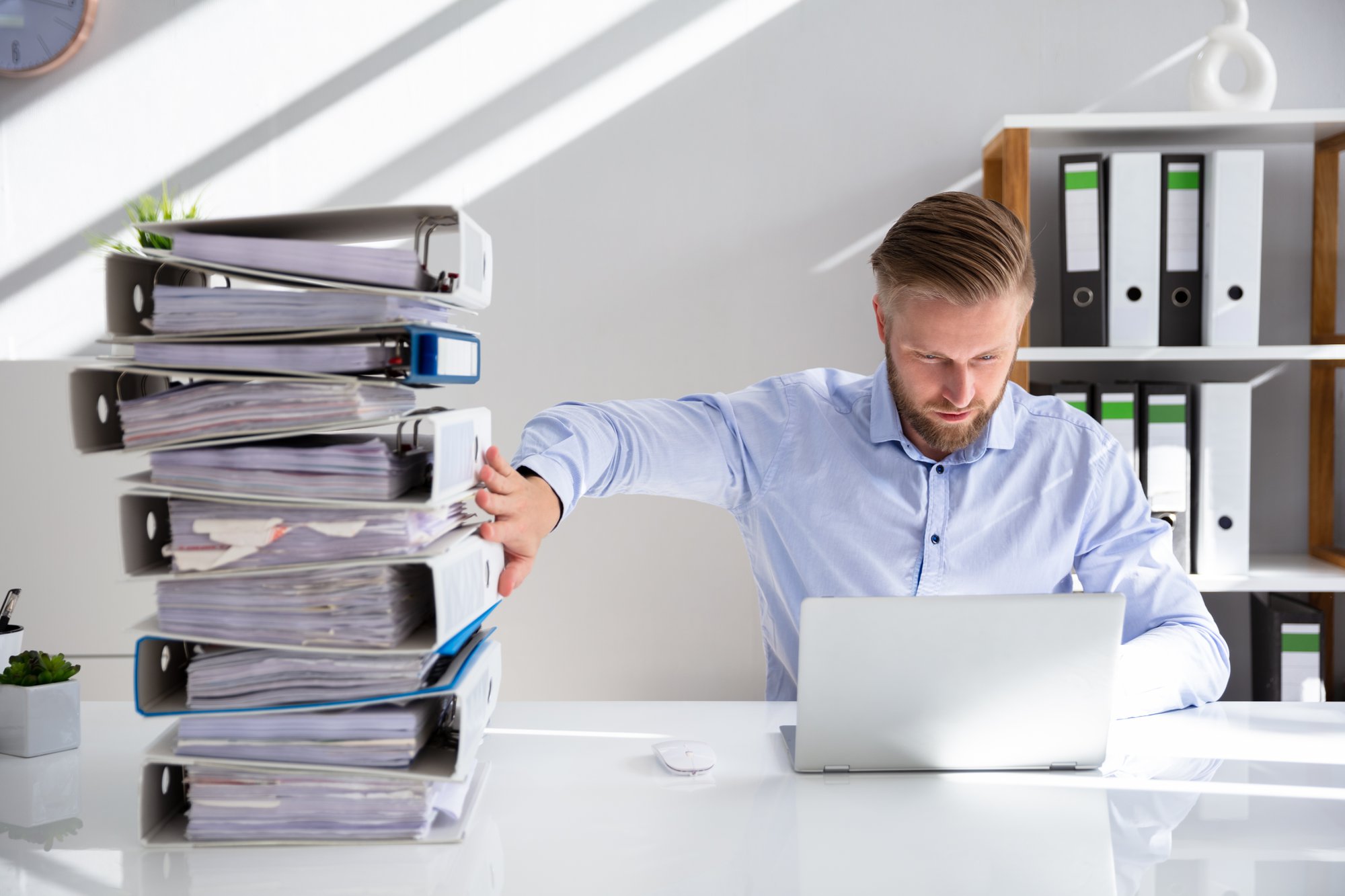 Office worker setting aside a tall stack of paper binders to work on a laptop
